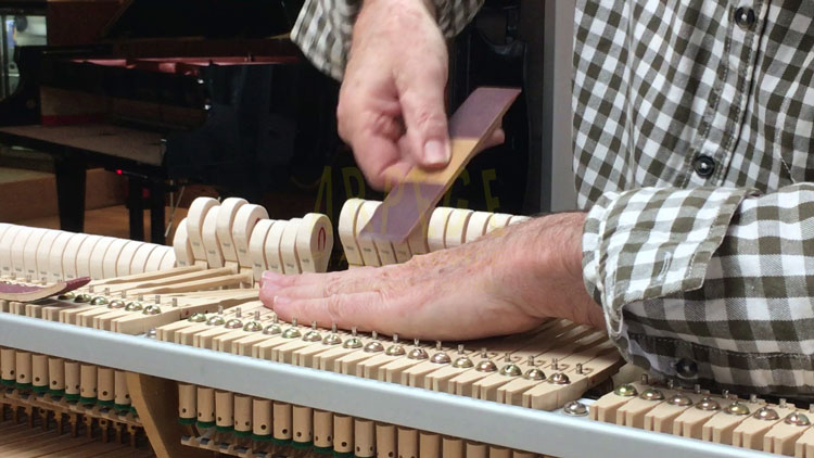 Ponçage préalable, avec une cale des têtes de marteaux d'un piano à queue, en vue de diminuer les empruntes de cordes